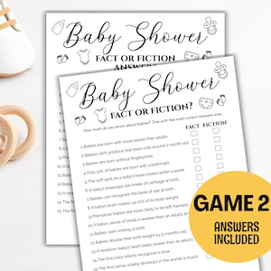 May include: Two white baby shower game sheets with the text "Baby Shower Fact or Fiction?" and a yellow circle with "Game 2 Answers Included." Also, a pair of white baby shoes and a wooden teething ring with gray beads.