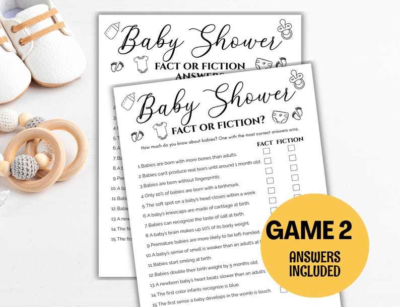 May include: Two white baby shower game sheets with the text "Baby Shower Fact or Fiction?" and a yellow circle with "Game 2 Answers Included." Also, a pair of white baby shoes and a wooden teething ring with gray beads.