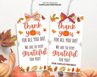 Könnte beinhalten: Zwei weiße Geschenkanhänger mit Herbstthema. Jeder Anhänger hat eine Kürbisillustration und die Worte "Danke für alles, was Sie tun! Wir sind Ihnen sehr dankbar!" Die Anhänger sind mit Herbstblättern verziert und mit einem Band gebunden.