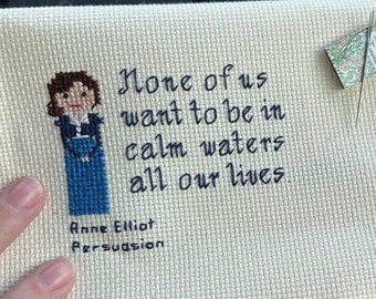 May include: Cross-stitch embroidery of a woman with brown hair and a blue dress. The quote "None of us want to be in calm waters all our lives." is stitched below the woman. The text "Anne Elliot Persuasion" is stitched below the quote.