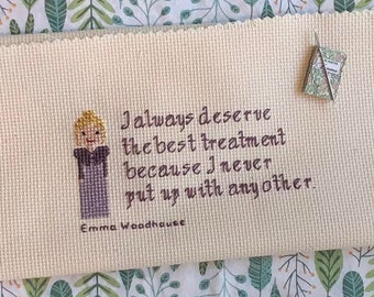 May include: A cross-stitch embroidery on beige fabric with a quote that reads "I always deserve the best treatment because I never put up with any other." The quote is attributed to Emma Woodhouse. A small embroidered figure of a woman with blonde hair and a purple dress is in the left corner of the image.