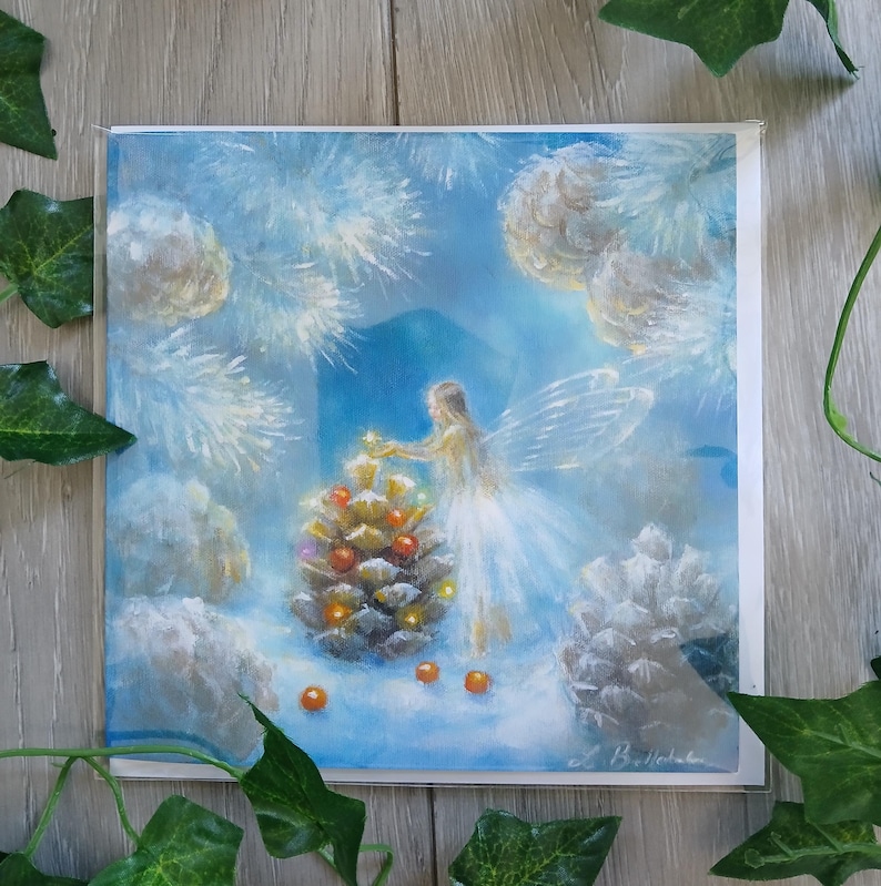 May include: A square art print featuring a fairy decorating a pinecone Christmas tree. The fairy is wearing a white dress and has translucent wings. The background is a winter scene with white snow and pinecones. The color palette is soft blues and whites.