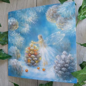 May include: An original painting of a fairy decorating a pinecone with orange ornaments. The fairy is wearing a white dress and has translucent wings. The background is a soft blue with white accents, and the painting is signed in the bottom right corner.