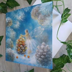 May include: A square painting depicts a fairy decorating a pine cone with ornaments. The fairy is wearing a white dress and has translucent wings. The background is a light blue with white accents, and the painting is on a white surface.