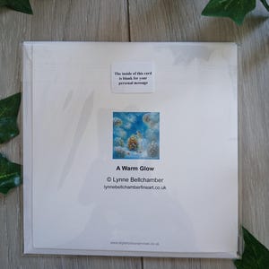 May include: A white greeting card in a clear plastic sleeve. The card features a small square image of pinecones and the text "A Warm Glow." The text "The inside of this card is blank for your personal message" is also visible.
