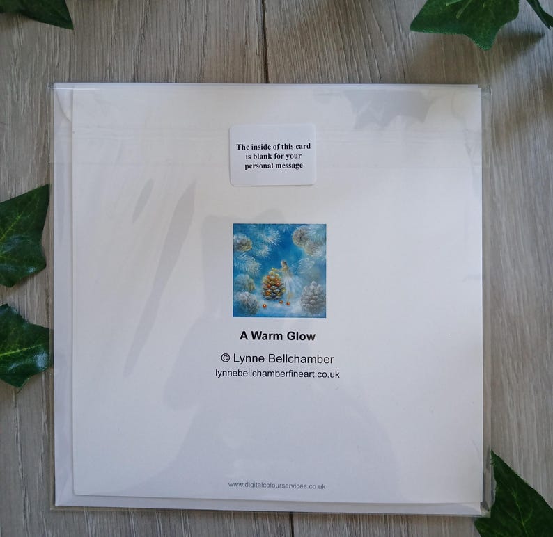 May include: A white greeting card in a clear plastic sleeve. The card features a small square image of pinecones and the text "A Warm Glow." The text "The inside of this card is blank for your personal message" is also visible.