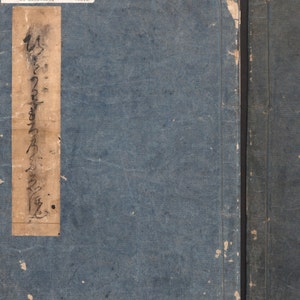 May include: A blue book cover with a tan label on the front. The label has Japanese writing on it and the text "A HUNDRED JAPANESE WOMEN BY MORONOBU, VOL. 2".