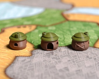 May include: Three small, brown, clay-like houses with green roofs and a chimney on top. The houses are sitting on a brown and white patterned surface.
