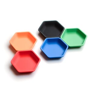 Puede incluir: Una colección de seis bandejas hexagonales en varios colores: rojo, naranja, negro, azul y verde. Las bandejas están vacías y parecen estar hechas de plástico o un material similar. Las bandejas están dispuestas en un grupo sobre una superficie blanca.