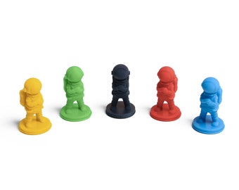 May include: Five astronaut game pieces in different colors: yellow, green, black, red, and blue. Each astronaut is standing on a round base.
