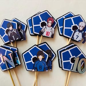 May include: A collection of cupcake toppers featuring anime-style characters. Each topper has a blue and white geometric design with a character illustration and a wooden stick. Some toppers have numbers.