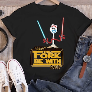 May include: Black t-shirt featuring a cartoon image of a fork character wielding two lightsabers. The text "May the Fork Be With You" is printed in yellow on the shirt.