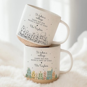 May include: Two white ceramic mugs stacked. Each mug features a village scene with colourful houses and the text "It takes a village, Thank you for being a part of ours, The Taylors."