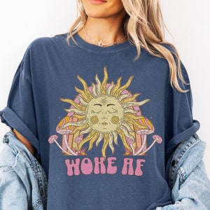 May include: A navy blue t-shirt with a graphic of a sun with closed eyes and mushrooms. The text "Woke AF" is printed below the graphic.