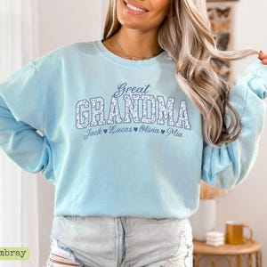Pu&ograve; includere: Una felpa azzurra con la scritta "Great Grandma" in un motivo floreale. Sotto ci sono i nomi Jack, Lucas, Olivia e Mia. La felpa &egrave; realizzata in un materiale morbido.