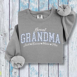 Pu&ograve; includere: Una felpa grigia con la scritta "Great Grandma" in bianco e lettere floreali. I nomi Jack, Lucas, Olivia e Mia sono stampati sotto. La felpa ha un girocollo e maniche lunghe.