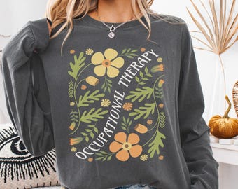 May include: A dark gray long-sleeved shirt with a floral design and the text "Occupational Therapy" in white.