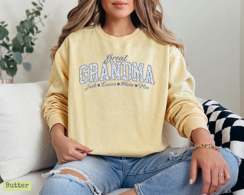 Pu&ograve; includere: Una felpa giallo chiaro con la scritta "Great Grandma" in un motivo floreale. Sotto, sono visualizzati i nomi Jack, Lucas, Olivia e Mia. La felpa &egrave; a maniche lunghe.