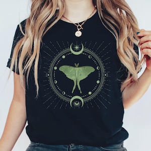 May include: A black t-shirt with a green luna moth graphic inside a circle with moons and stars. The graphic is surrounded by a circle of smaller moons and stars.