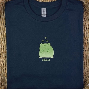 May include: A black t-shirt featuring a green frog graphic with the word "ribbit" printed underneath.
