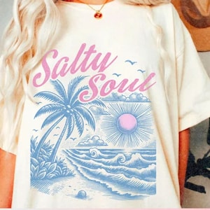 May include: White t-shirt with a graphic of a palm tree, ocean waves, and a sun with the text "Salty Soul" in pink lettering.