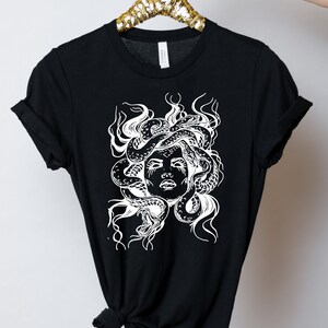 May include: Black t-shirt with a white graphic of Medusa, a mythical Greek figure with snakes for hair.