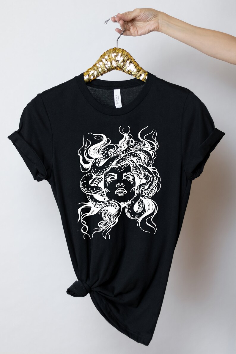 May include: Black t-shirt with a white graphic of Medusa, a mythical Greek figure with snakes for hair.