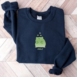 May include: A navy blue sweatshirt with a green frog graphic and the word "ribbit" printed below. The frog is surrounded by small white stars.
