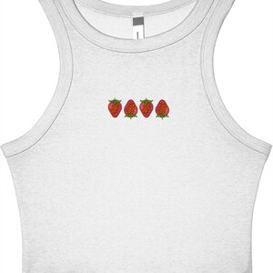 May include: A white tank top with a scoop neck and embroidered strawberries. The strawberries are red with green leaves and are arranged in a horizontal line across the chest. The tank top is made of a soft, lightweight material.