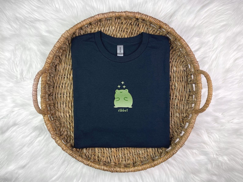 May include: A black t-shirt featuring a green frog graphic with the word "ribbit" printed underneath.