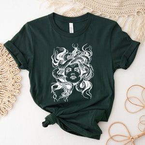 May include: A dark green t-shirt with a white graphic print of Medusa, a mythical Greek figure with snakes for hair.
