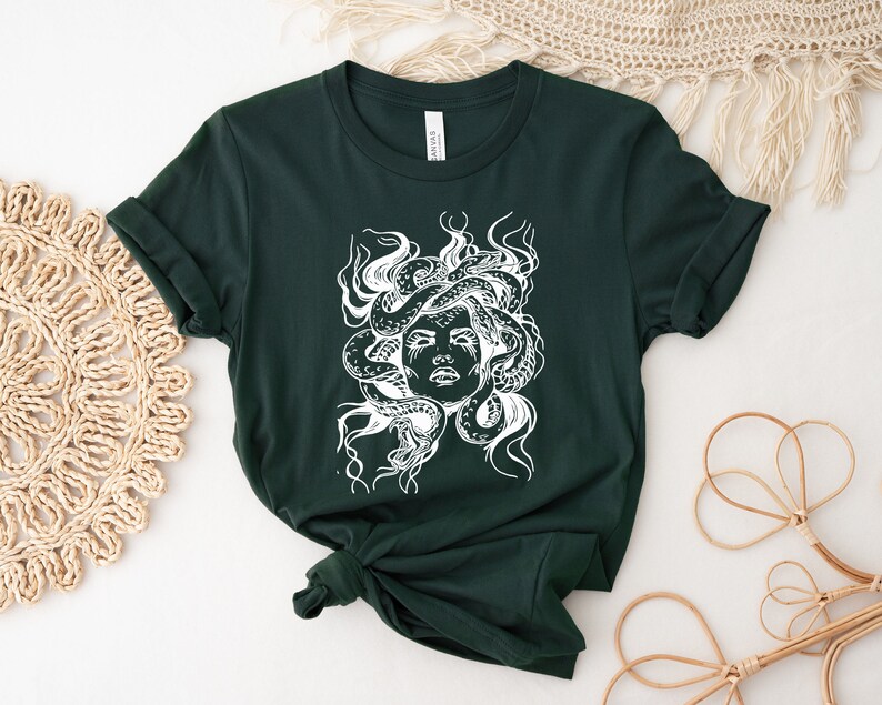 May include: A dark green t-shirt with a white graphic print of Medusa, a mythical Greek figure with snakes for hair.