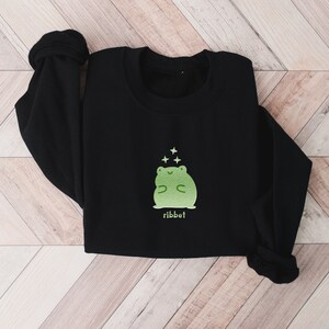May include: Black sweatshirt with a green frog graphic and the word "ribbit" printed below. The frog is smiling and has stars above its head.