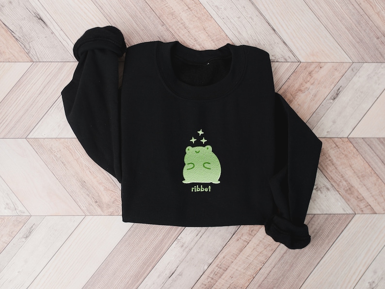 May include: Black sweatshirt with a green frog graphic and the word "ribbit" printed below. The frog is smiling and has stars above its head.