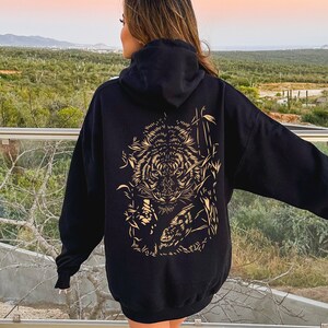 May include: Black hoodie with a gold tiger graphic on the back. The tiger is surrounded by bamboo and other foliage.