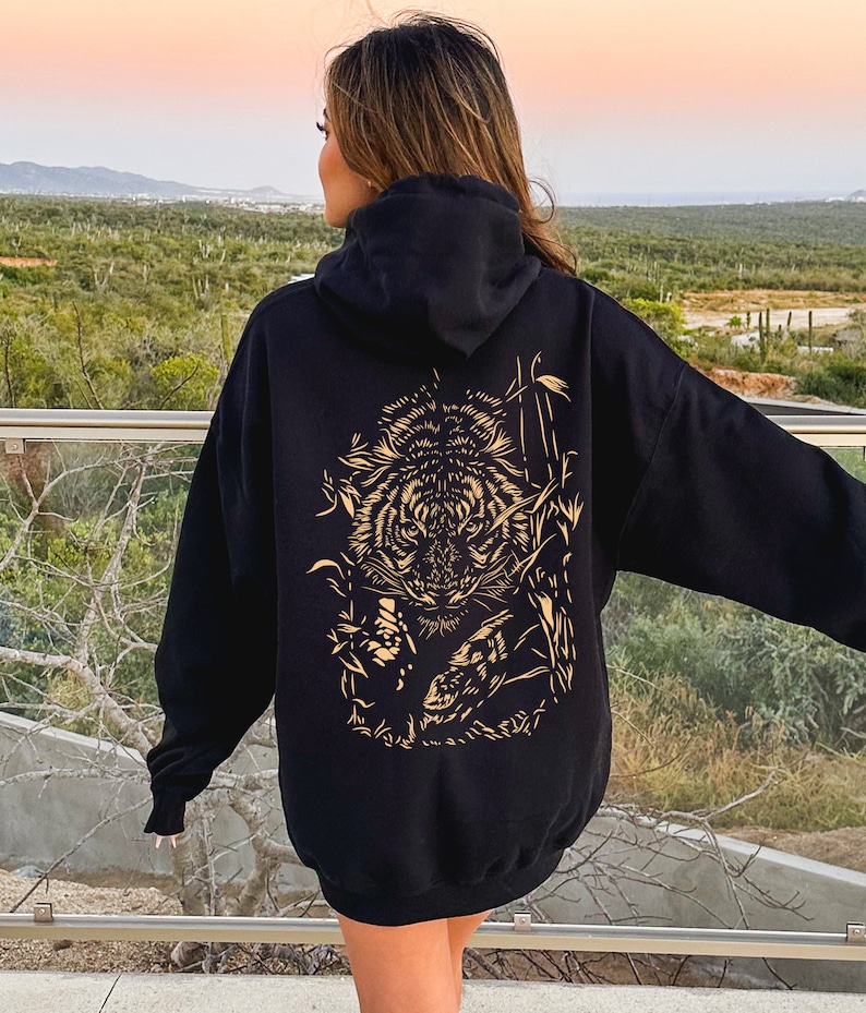 May include: Black hoodie with a gold tiger graphic on the back. The tiger is surrounded by bamboo and other foliage.
