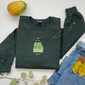 May include: A dark green sweatshirt with a light green frog graphic and the word "ribbit" printed below. The frog is surrounded by small white stars.