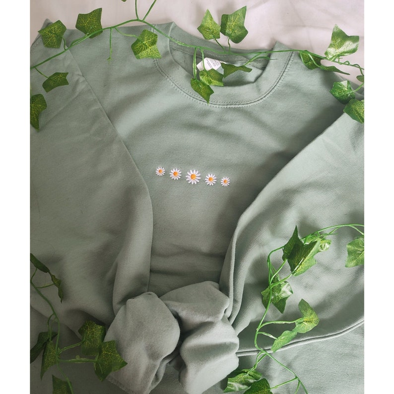 May include: A sage green sweatshirt with a row of embroidered white daisies.