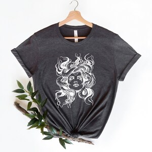 May include: A dark gray t-shirt with a white graphic of Medusa, a mythical Greek figure with snakes for hair.