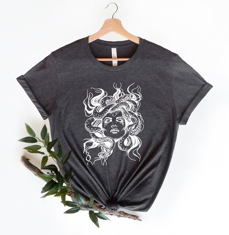 May include: A dark gray t-shirt with a white graphic of Medusa, a mythical Greek figure with snakes for hair.