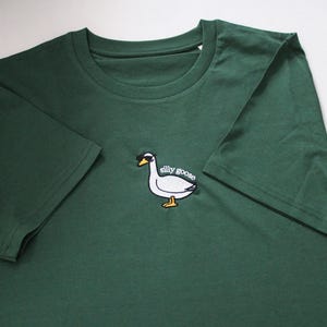 May include: A dark green t-shirt with an embroidered white goose wearing sunglasses and the text "silly goose".