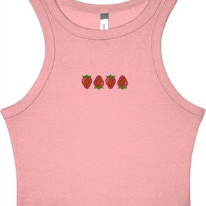 May include: A light pink crop top with a scoop neck and a row of four embroidered strawberries across the chest. The strawberries are red with green leaves. The top is sleeveless.