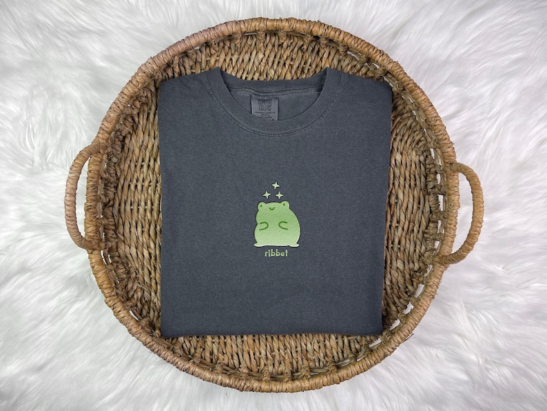 May include: A dark gray t-shirt with a green frog graphic and the word "ribbit" printed below it.