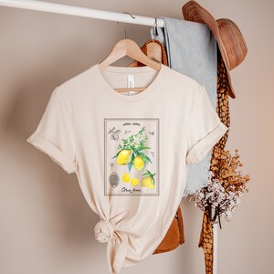K&ouml;nnte beinhalten: Ein beiges T-Shirt mit einer Vintage-botanischen Illustration von Zitronen und Bl&auml;ttern. Die Illustration ist gerahmt und enth&auml;lt den Text "Citrus Limon".