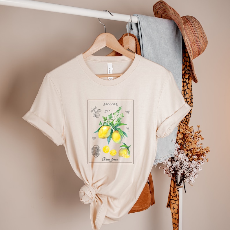 K&ouml;nnte beinhalten: Ein beiges T-Shirt mit einer Vintage-botanischen Illustration von Zitronen und Bl&auml;ttern. Die Illustration ist gerahmt und enth&auml;lt den Text "Citrus Limon".