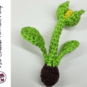 May include: A crocheted green plant with a brown bulb and a yellow flower. The plant has three leaves and the flower is open.