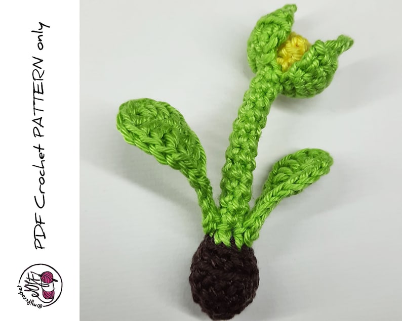 May include: A crocheted green plant with a brown bulb and a yellow flower. The plant has three leaves and the flower is open.