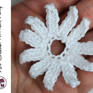 May include: A white crocheted flower with a center hole. The flower has 10 petals and is made with a single crochet stitch.