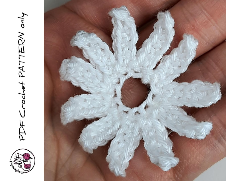May include: A white crocheted flower with a center hole. The flower has 10 petals and is made with a single crochet stitch.