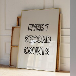May include: A white framed poster with the text "EVERY SECOND COUNTS" in black outlined letters. The poster is leaning against a white wall with gold trim.